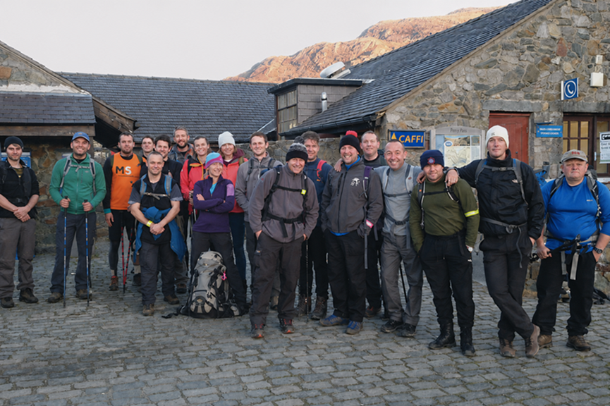 A group of hikers and their maximum adventure guides smiling together outside a stone building during a guided adventure.