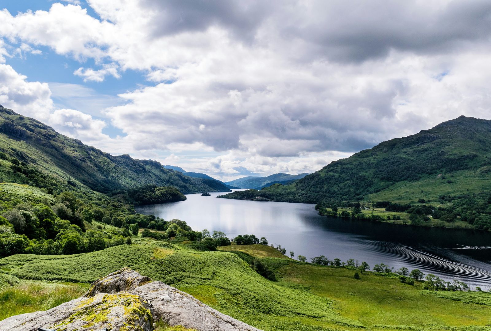 A view of a large body of water (a loch), with green hills and mountains surrounding it on either side.